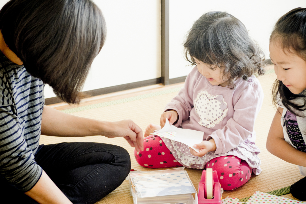 Two little girls are playing with mother at home. They are playing Jaoanese traditional origami.
